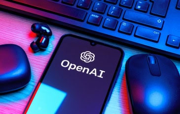 Logo da OpenAI em um smartphone que está rodeado por um fone de ouvido, um mouse e um teclado