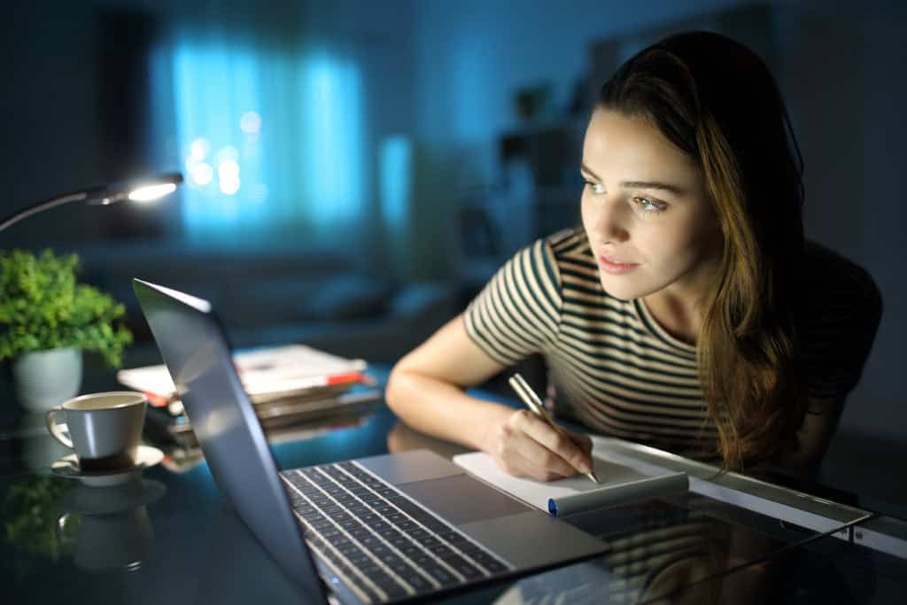 Mulher em um escritório escrevendo em caderno na frente do notebook em uma mesa