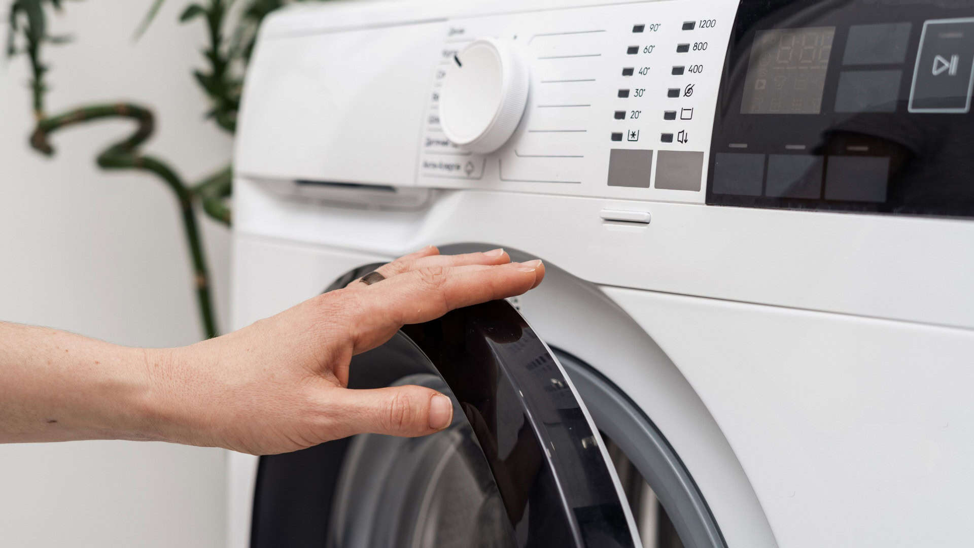 Mulher abre ou fecha a porta de máquina de lavar automática com painel digital moderno