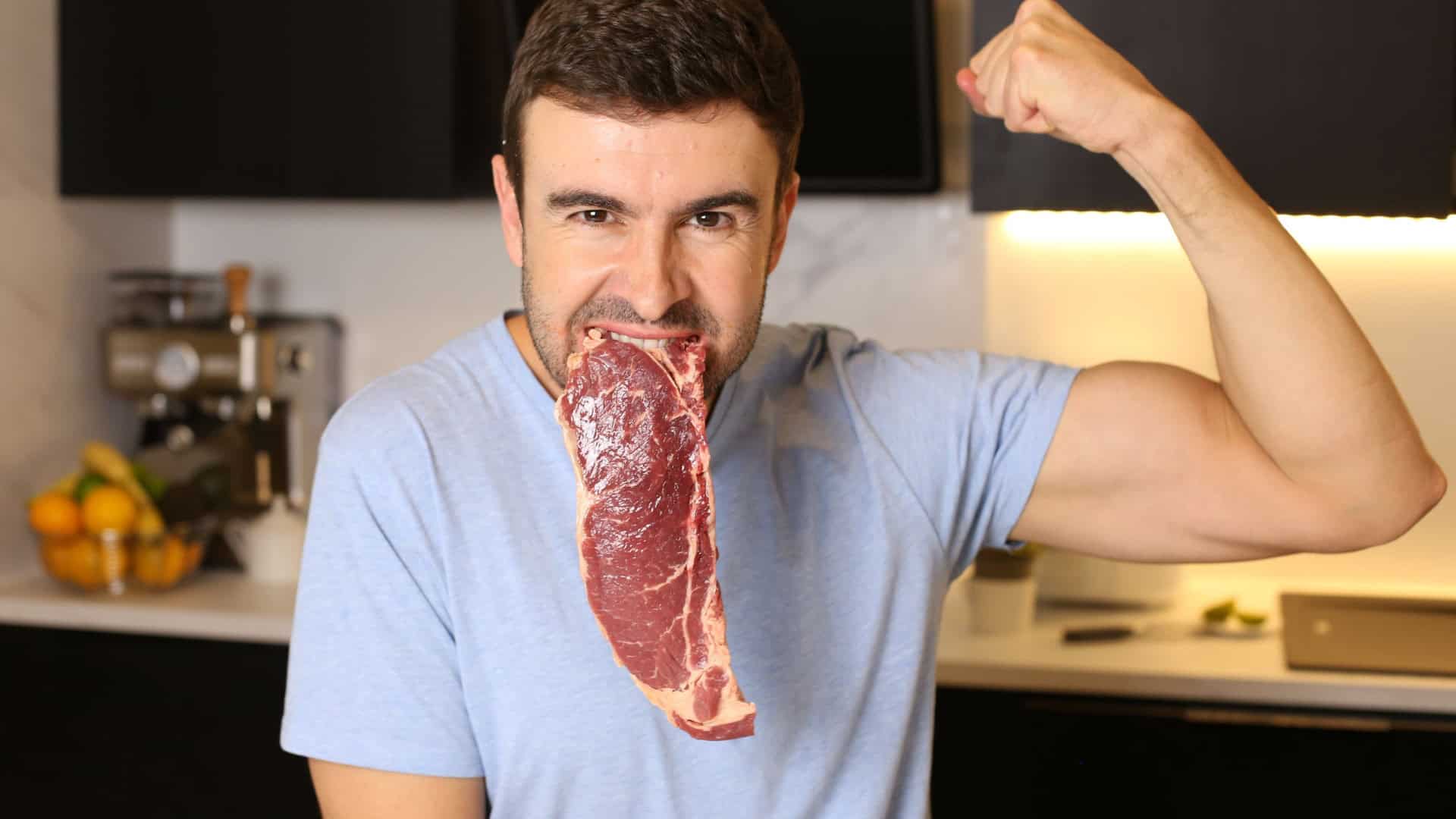 Homem com um bife cru na boca enquanto mostra os músculos do braço