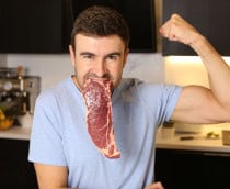 Homem com um bife cru na boca enquanto mostra os músculos do braço