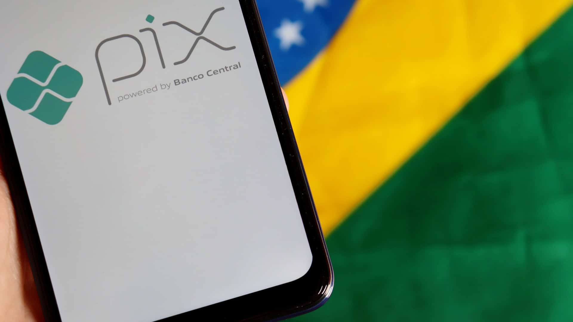 Ao fundo, bandeira do Brasil; à frente, smartphone exibindo, em sua tela, o logo do Pix