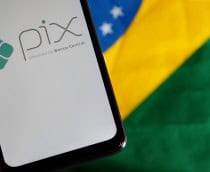Ao fundo, bandeira do Brasil; à frente, smartphone exibindo, em sua tela, o logo do Pix
