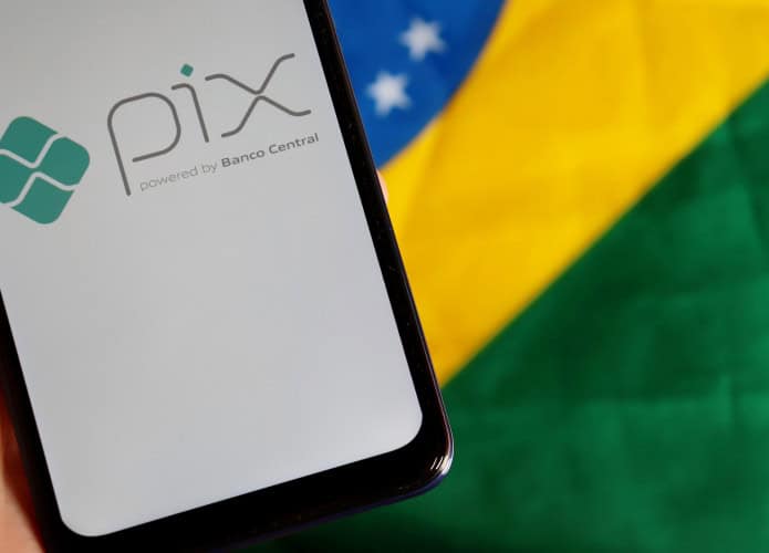 Ao fundo, bandeira do Brasil; à frente, smartphone exibindo, em sua tela, o logo do Pix