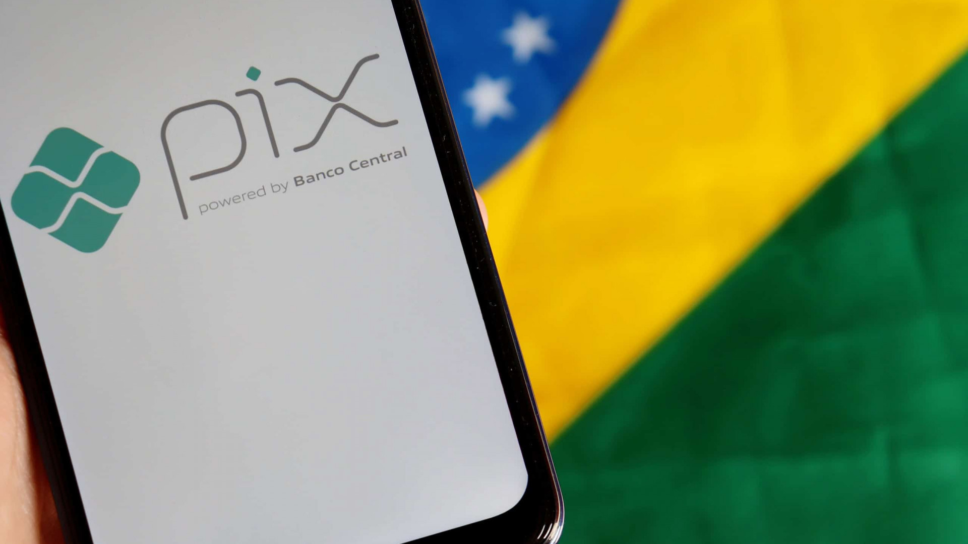 Ao fundo, bandeira do Brasil; à frente, smartphone exibindo, em sua tela, o logo do Pix