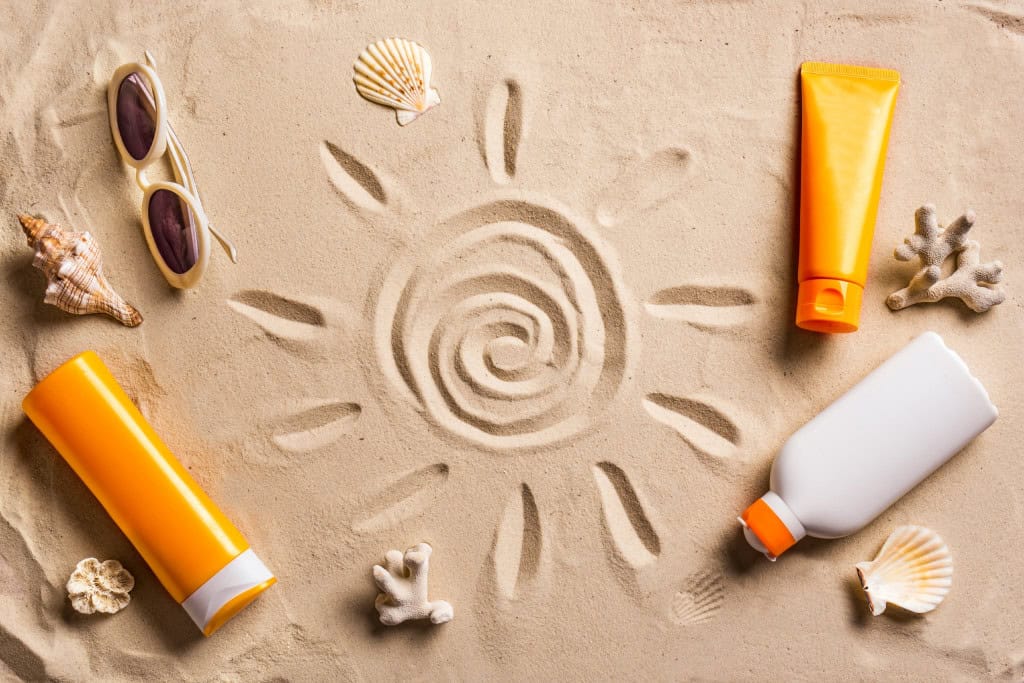 Desenho do Sol feito na areia e com vários tipos de protetores solares ao redor