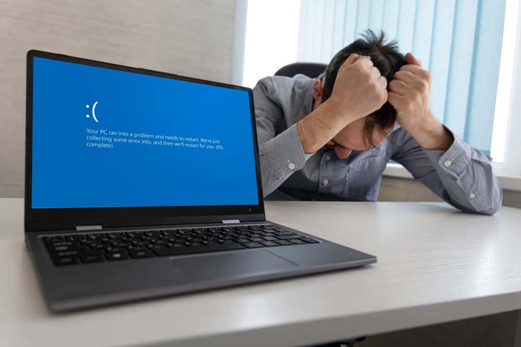 Imagem mostrando tela azul de erro no laptop contra o fundo de um homem chateado e irritado segurando a cabeça