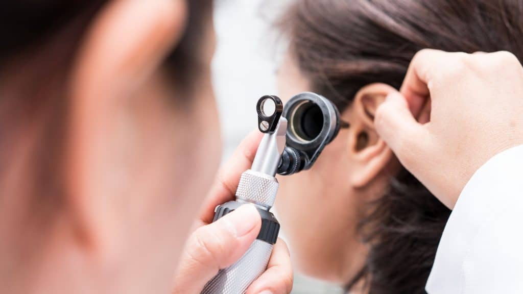 Médico examinando o ouvido do paciente com otoscópio, sugerindo possível problema auditivo