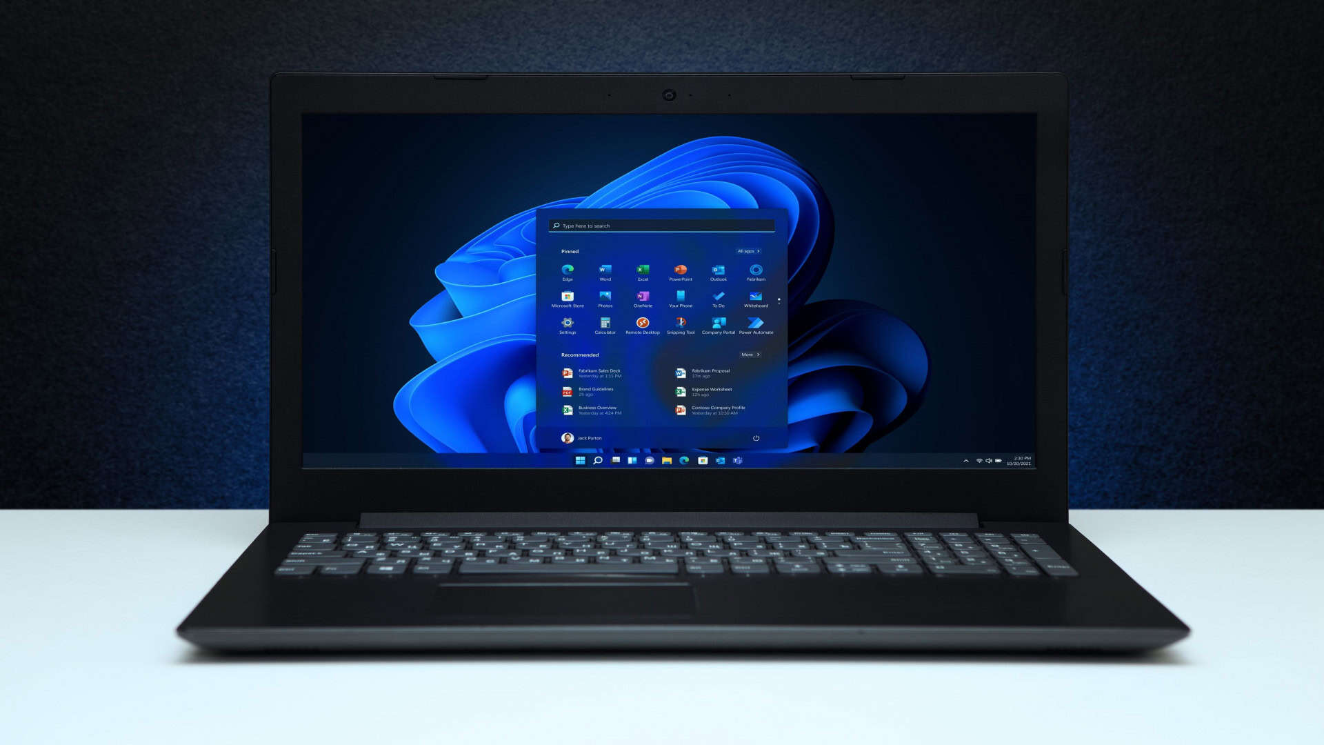Imagem mostra área de trabalho do Windows 11 com logotipo na tela de um laptop em uma parede texturizada preta com luz azul.