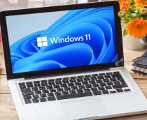 Imagem ilustrativa de logotipo oficial da marca Windows 11 na tela de um laptop em mesa de escritório