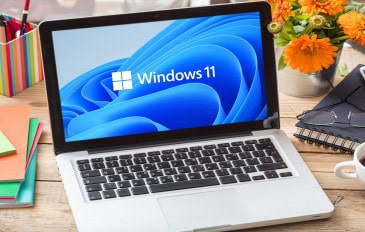 Imagem ilustrativa de logotipo oficial da marca Windows 11 na tela de um laptop em mesa de escritório