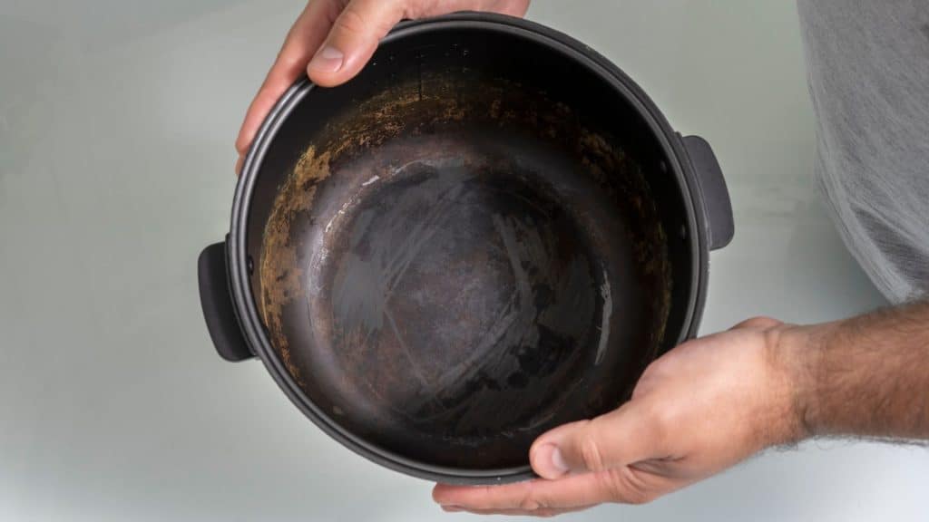 Mãos de homem segurando uma panela que está velha por dentro, com material descascado.