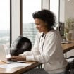 Empresária afro-americana sorrindo, usando laptop, trabalhando em projeto online em casa, sentada à mesa de madeira com capacete de motocicleta, jovem conversando ou comprando online, navegando em aplicativos
