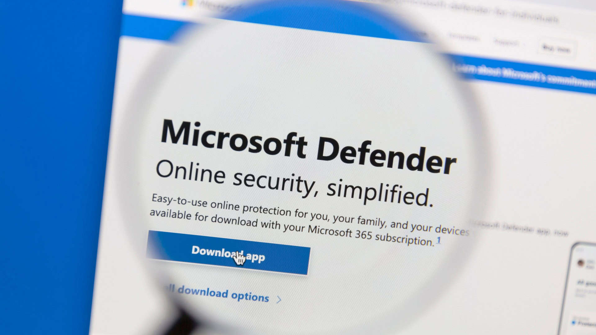 Tela de computador mostra o site do Microsoft Defender com uma lupa destacando o texto “Segurança online simplificada” e botão “Download APP”.
