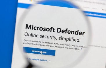 Tela de computador mostra o site do Microsoft Defender com uma lupa destacando o texto “Segurança online simplificada” e botão “Download APP”.