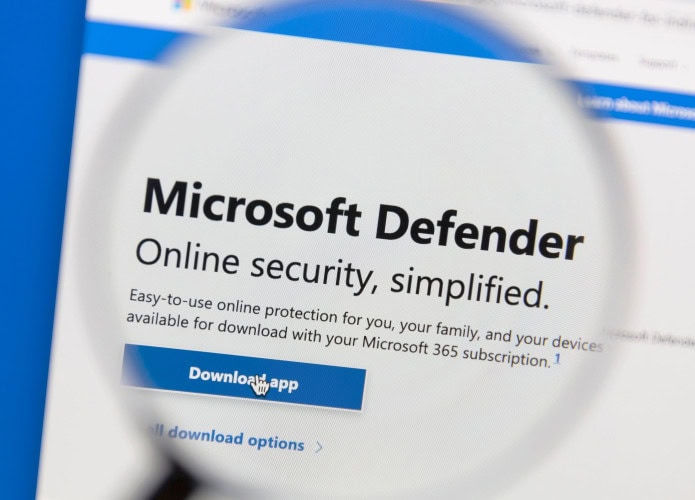 Tela de computador mostra o site do Microsoft Defender com uma lupa destacando o texto “Segurança online simplificada” e botão “Download APP”.
