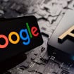 Celular com logotipo do Google na tela colocado na frente de tela exibindo ilustração de chip de inteligência artificial (IA)
