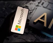 Pessoa segurando celular com logotipo da Microsoft na tela na frente de outra tela, esta grande, exibindo ilustração de chip de inteligência artificial (IA)