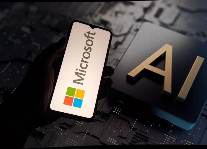Pessoa segurando celular com logotipo da Microsoft na tela na frente de outra tela, esta grande, exibindo ilustração de chip de inteligência artificial (IA)