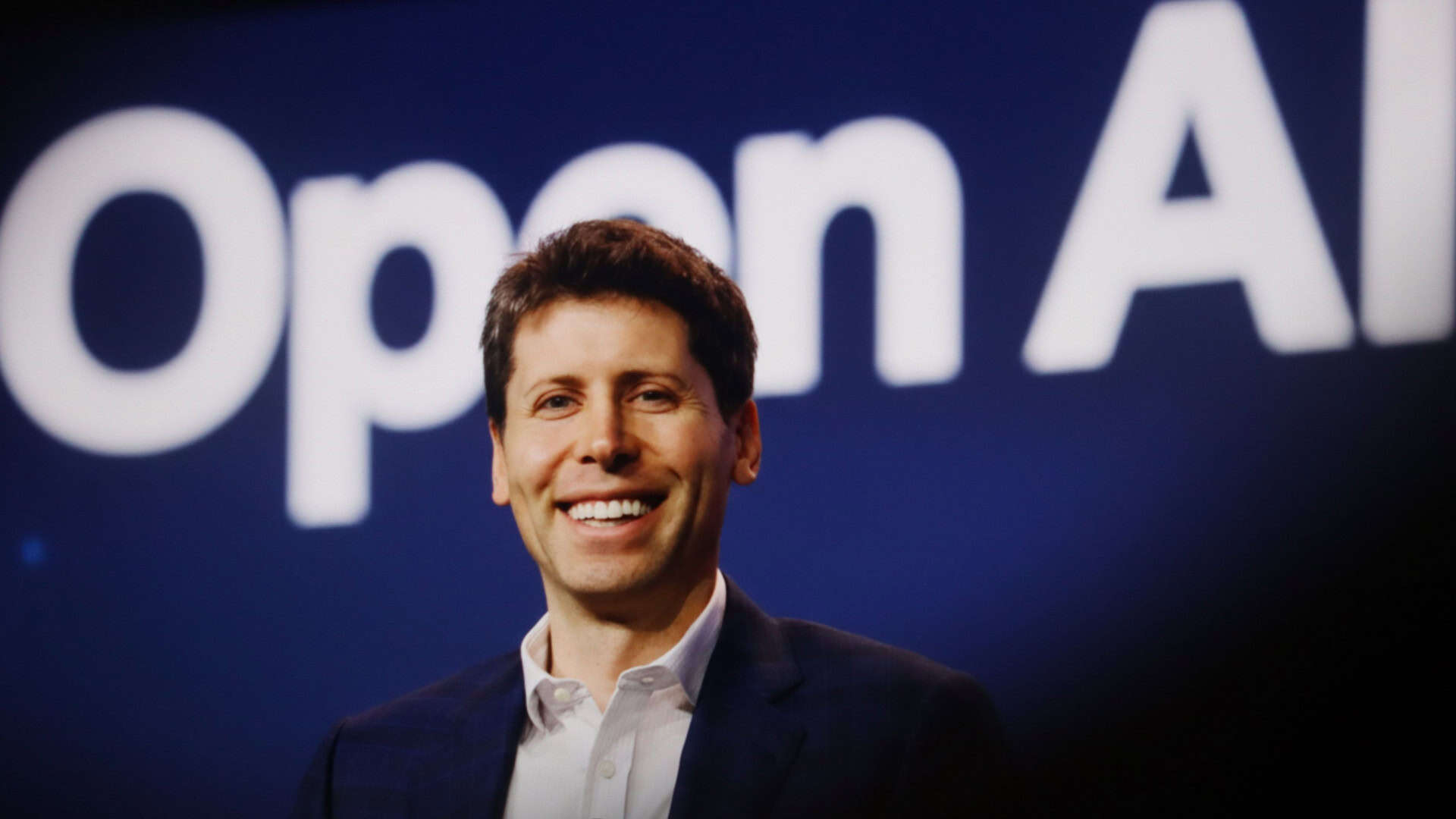 Sam Altman sorrindo em frente letreiro onde está escrito OpenAI