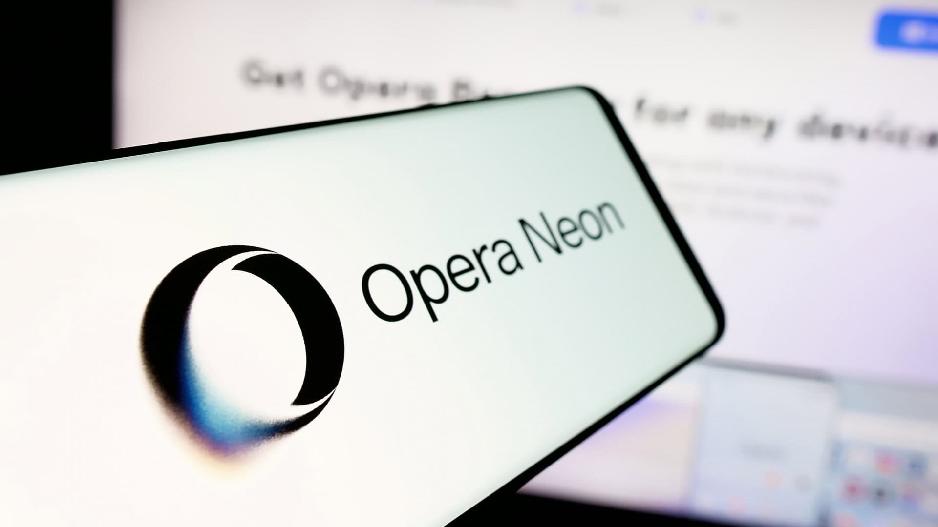 Celular com logotipo do Opera Neon na tela na frente de tela de computador com página sobre o navegador aberta