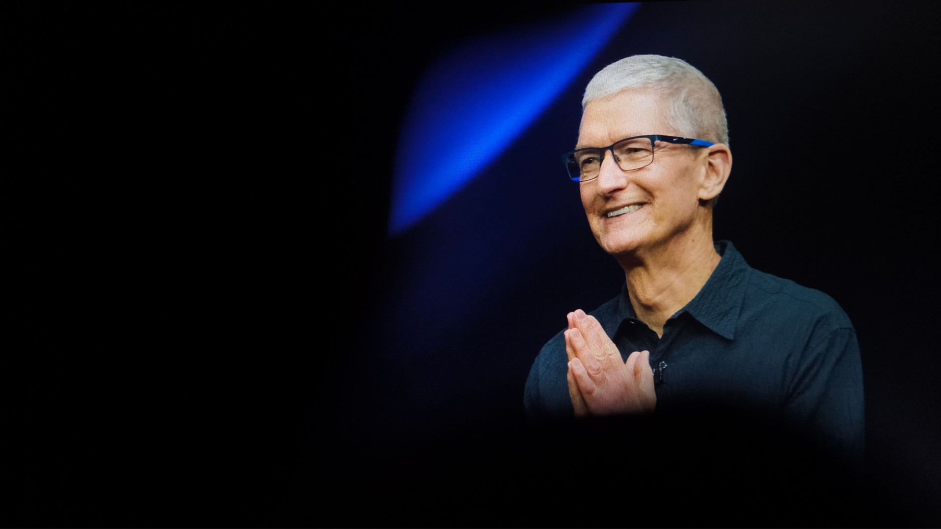 CEO da Apple, Tim Cook, olhando para o lado e sorrindo, com mãos juntas em gesto de gratidão
