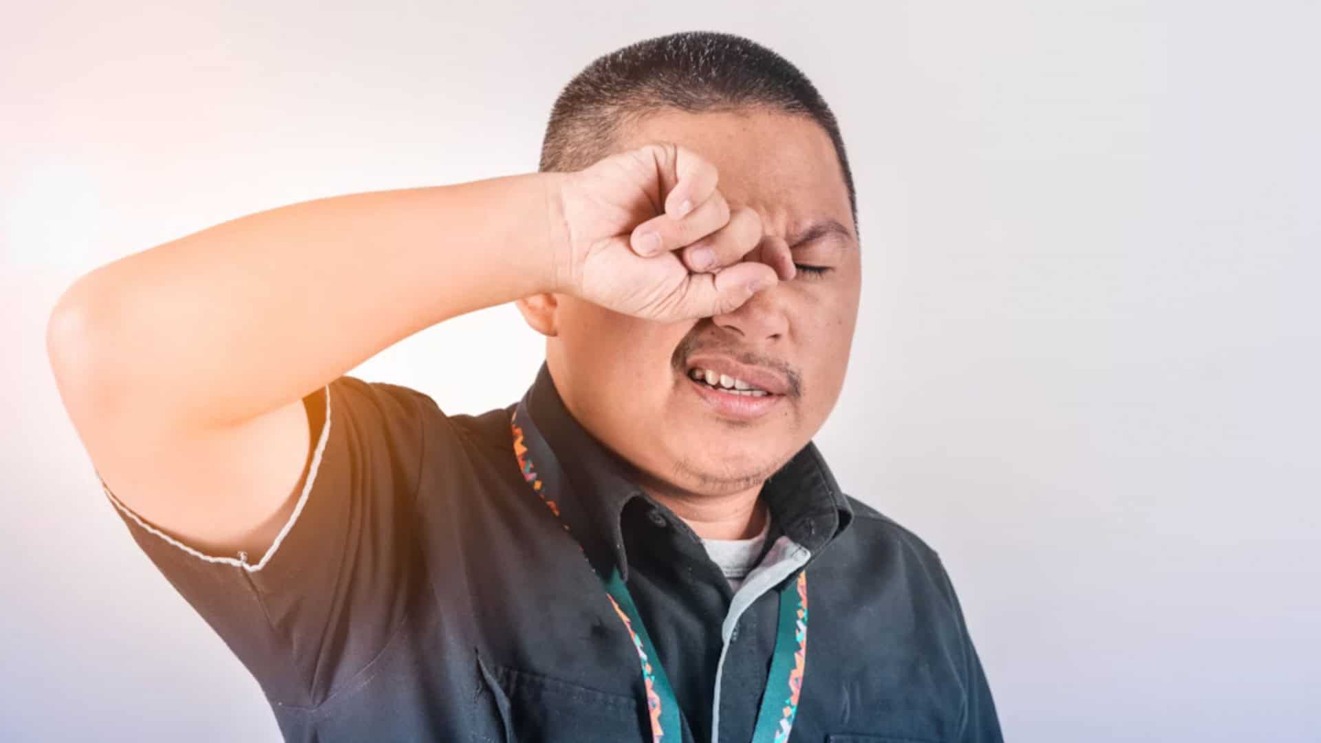 Homem de camisa preta coçando o olho direito com a mão direita