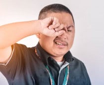 Homem de camisa preta coçando o olho direito com a mão direita