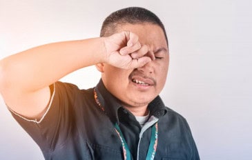 Homem de camisa preta coçando o olho direito com a mão direita