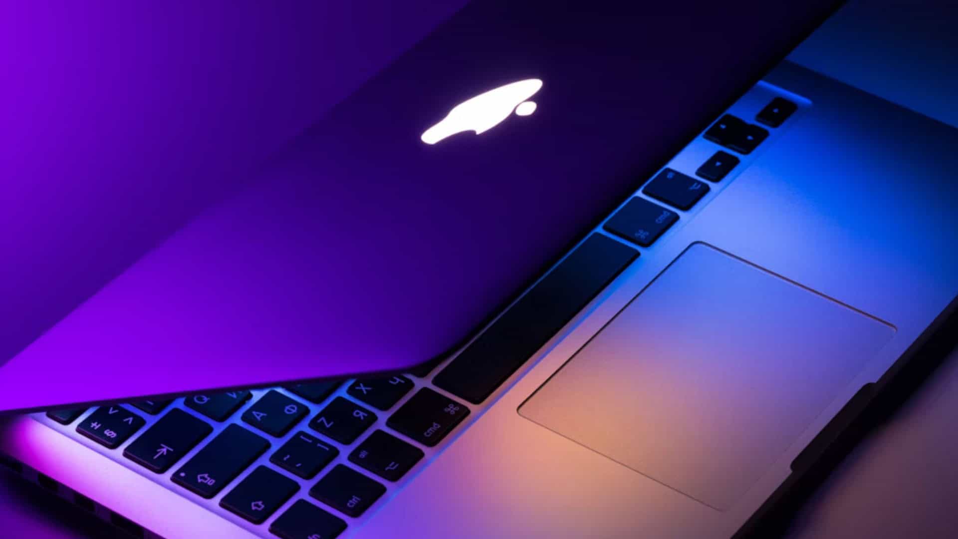 MacBook parcialmente fechado em cima de uma mesa, emitindo luzes coloridas