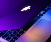 MacBook parcialmente fechado em cima de uma mesa, emitindo luzes coloridas