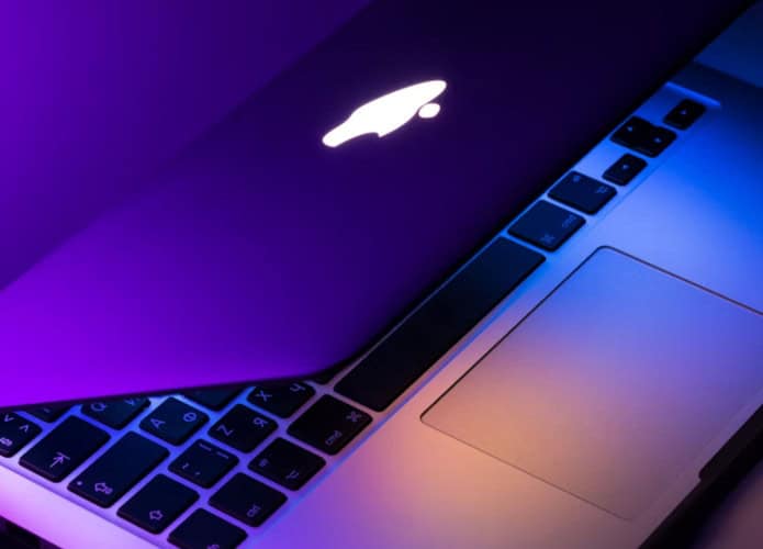 MacBook parcialmente fechado em cima de uma mesa, emitindo luzes coloridas