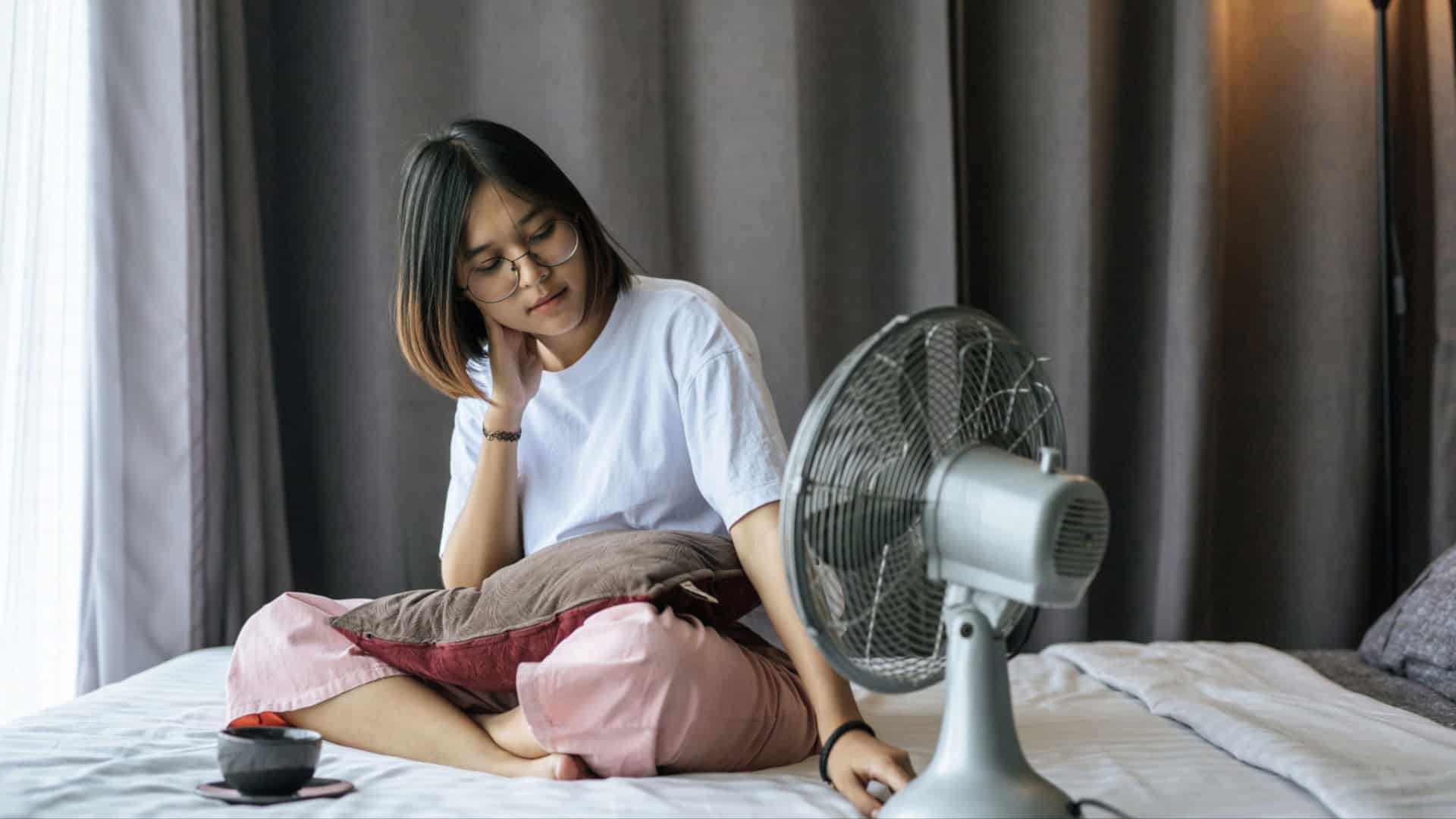 Garota sentada na cama controla ventilador