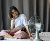 Garota sentada na cama controla ventilador