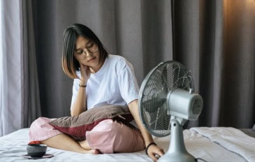 Garota sentada na cama controla ventilador