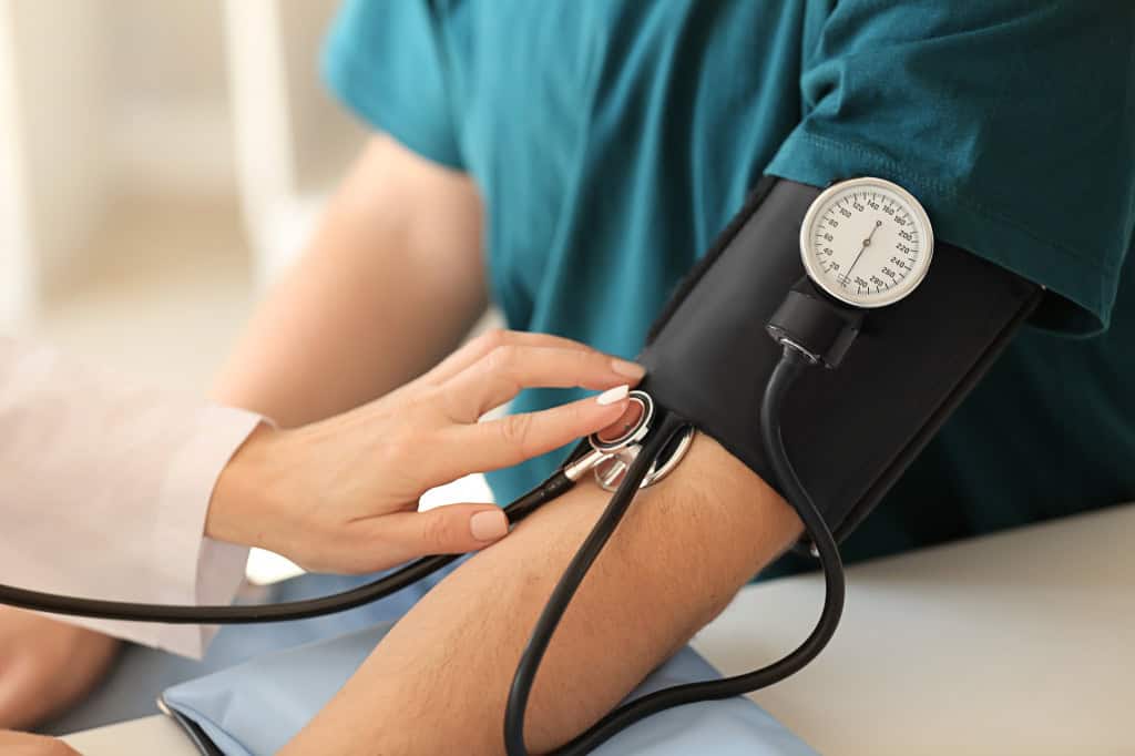 Profissional de saúde mede pressão arterial com esfigmomanômetro manual no braço de um paciente.