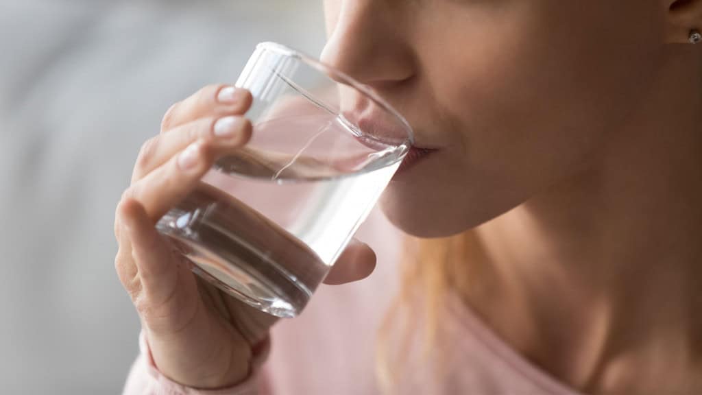 Close-up de mulher com sede segurando um copo e bebendo água para evitar a desidratação e manter o equilíbrio do corpo