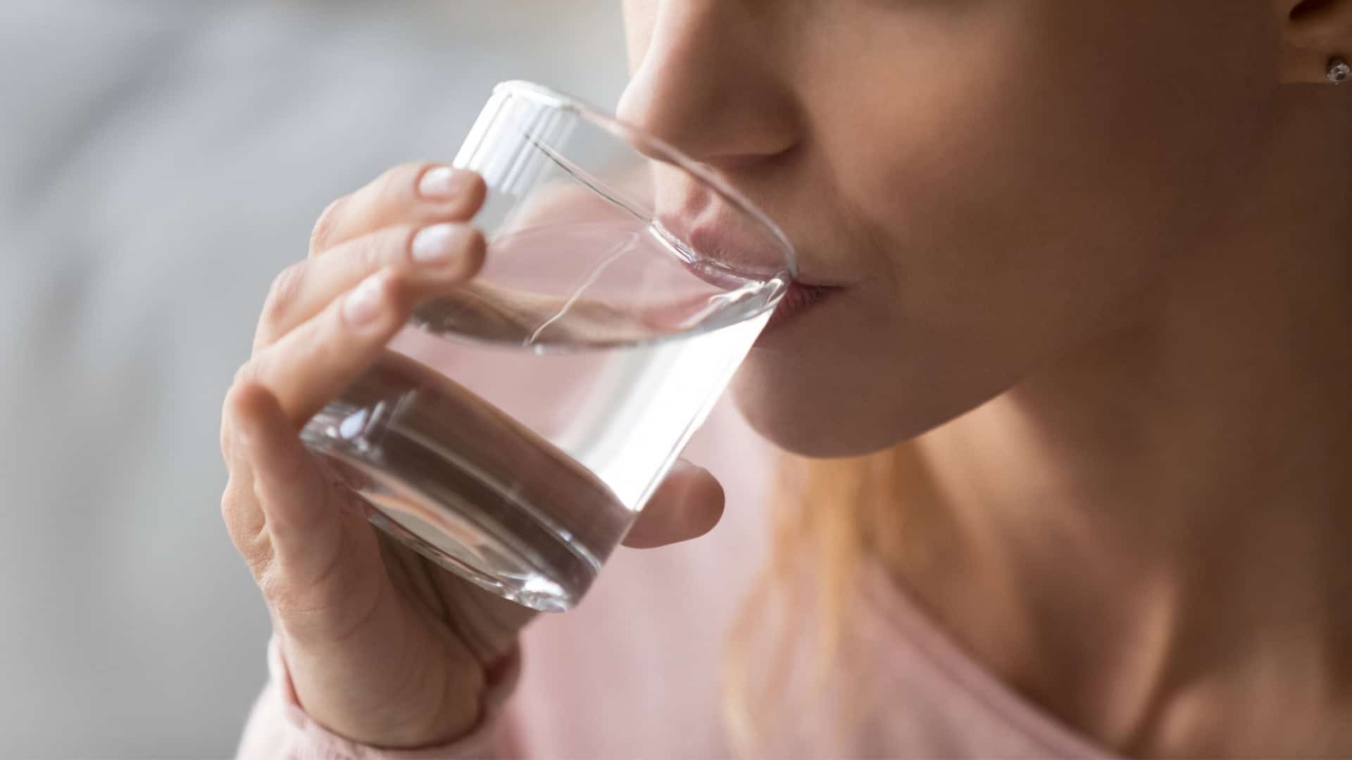 Close-up de mulher com sede segurando um copo e bebendo água para evitar a desidratação e manter o equilíbrio do corpo