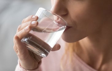 Close-up de mulher com sede segurando um copo e bebendo água para evitar a desidratação e manter o equilíbrio do corpo