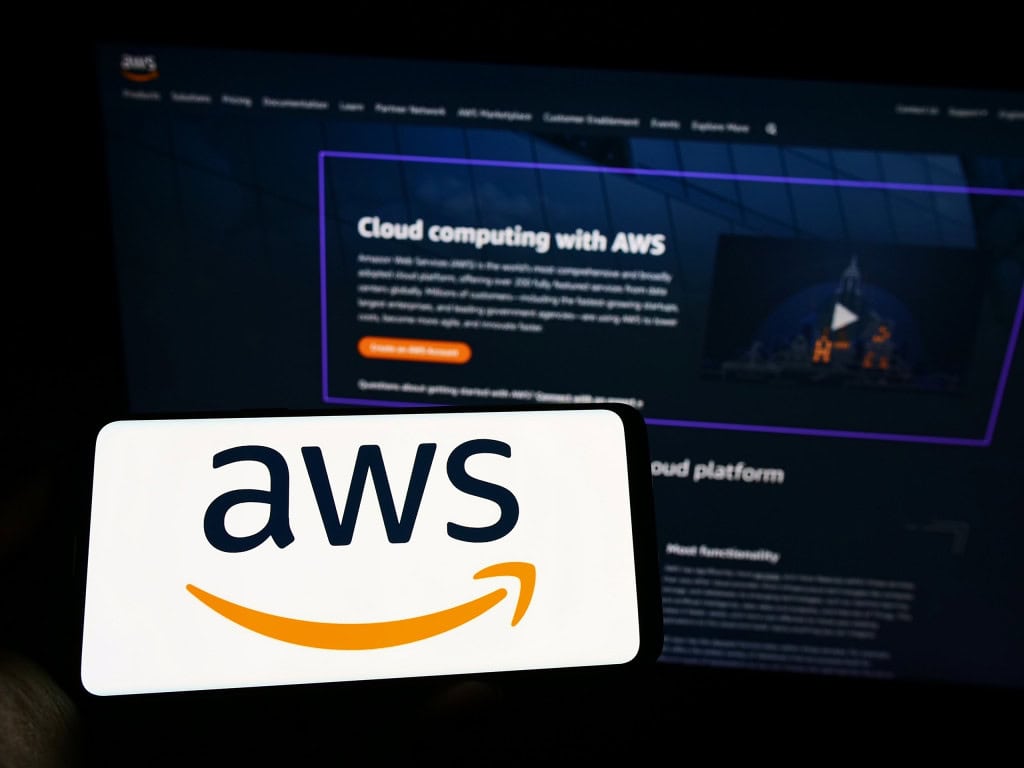 Ao fundo, site da AWS; à frente, smartphone na horizontal com o logo da AWS