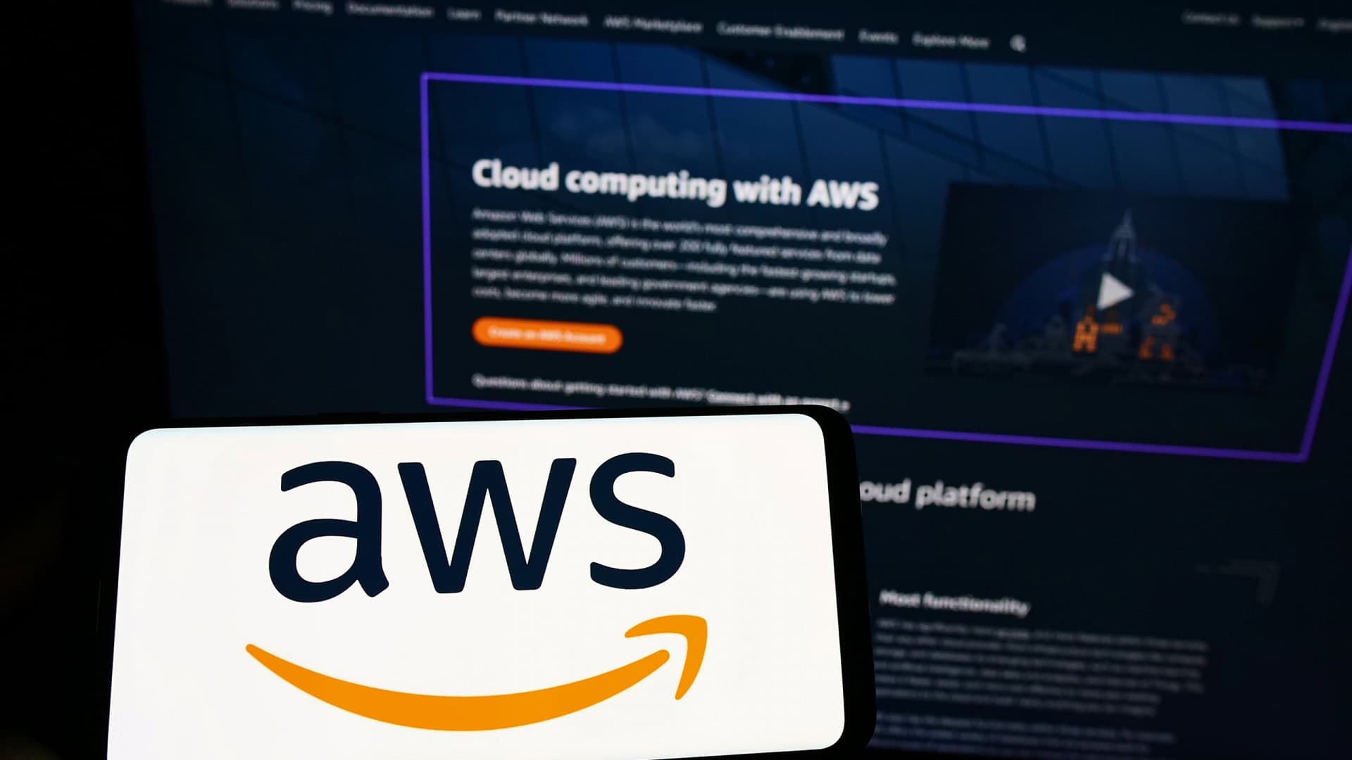 Ao fundo, site da AWS; à frente, smartphone na horizontal com o logo da AWS