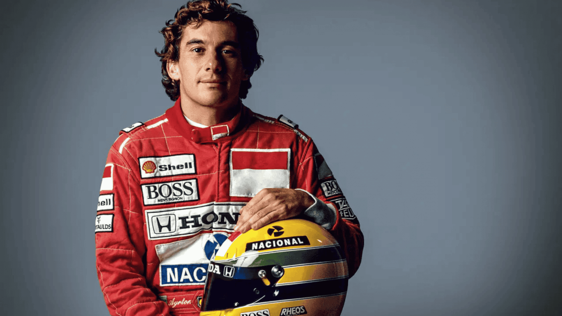 Ayrton Senna, rei do GP de Mônaco, segurando um capacete amarelo com faixas verde e azul, posando de frente e com expressão séria.