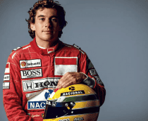 Ayrton Senna, rei do GP de Mônaco, segurando um capacete amarelo com faixas verde e azul, posando de frente e com expressão séria.