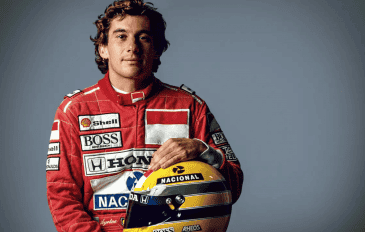 Ayrton Senna, rei do GP de Mônaco, segurando um capacete amarelo com faixas verde e azul, posando de frente e com expressão séria.