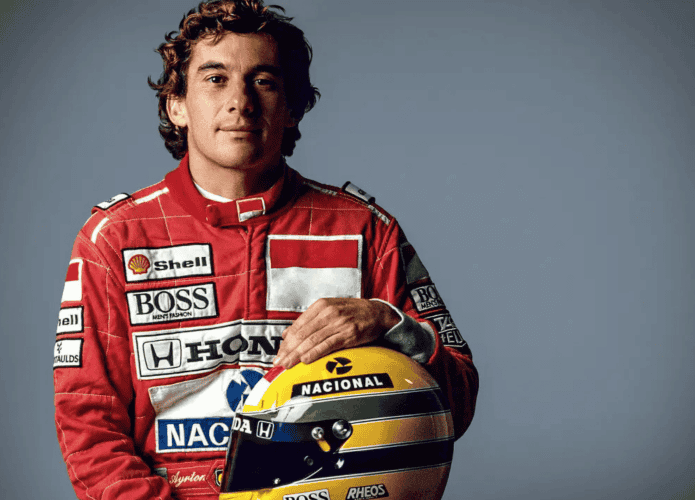 Ayrton Senna, rei do GP de Mônaco, segurando um capacete amarelo com faixas verde e azul, posando de frente e com expressão séria.