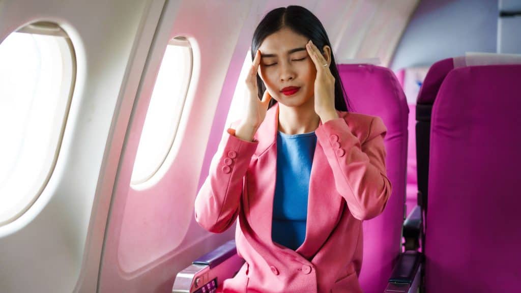 Passageira asiática sentada próxima à janela durante o voo, sentindo dor devido à variação de pressão.