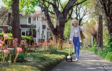 Mulher caminhando por uma calçada arborizada com a bengala inteligente Glide.