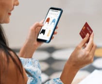 Mulher segurando com a mão esquerda e olhando para um smartphone e com um cartão na mão direita