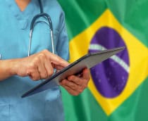 imagem mostra um médico mexendo em um tablet em frente a uma bandeira do brasil