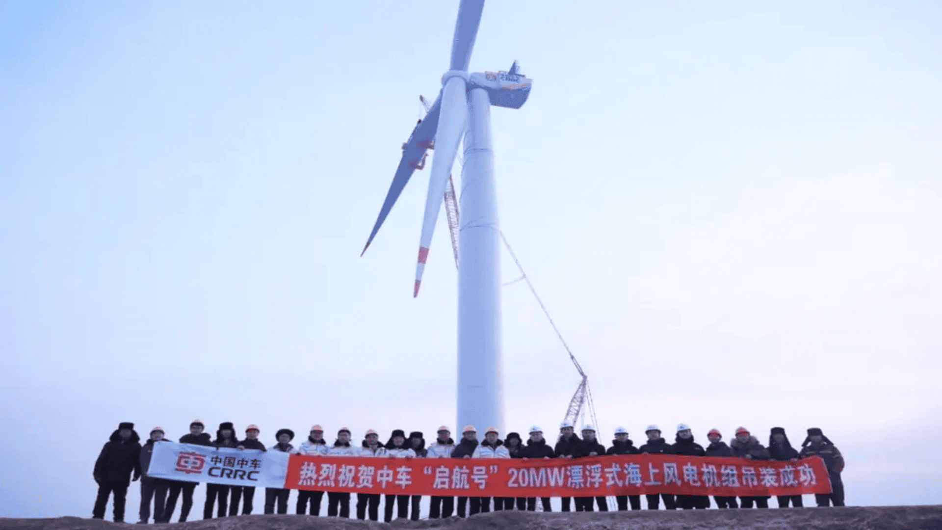 Pessoas segurando cartazes à frente de uma turbina eólica